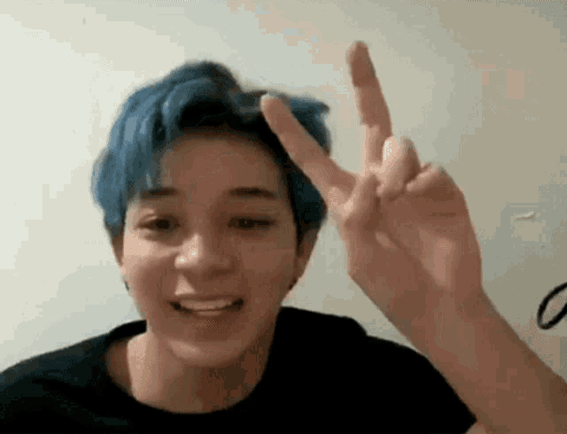 a young man with blue hair is making a peace sign with his hands .