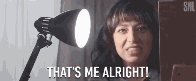 a woman is sitting in front of a lamp and says that 's me alright !