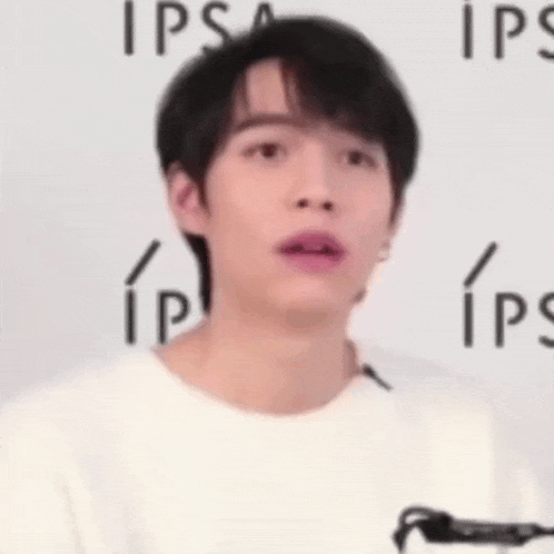 a young man wearing a white t-shirt is standing in front of a wall with ips written on it .