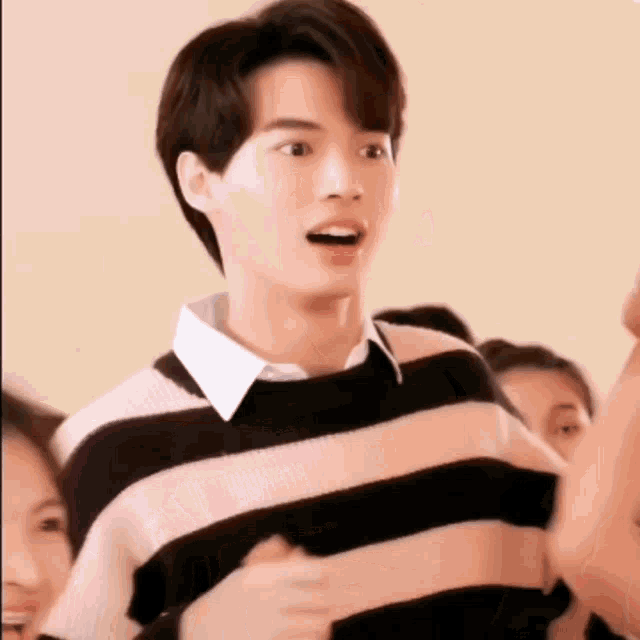 a young man wearing a pink and black striped sweater is standing in a crowd .