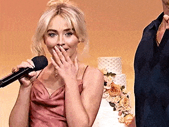 a woman in a pink dress is holding a microphone and covering her mouth .