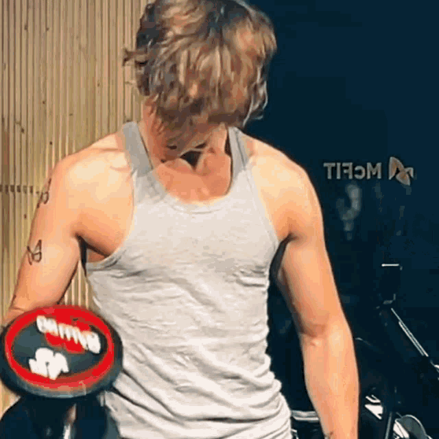 a man in a grey tank top is lifting a red dumbbell with the word clipper on it .