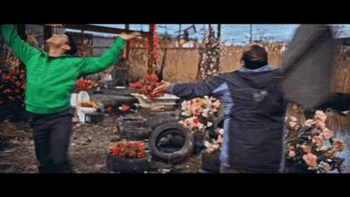 a woman in a green sweater and a man in a blue jacket are dancing in a field of flowers