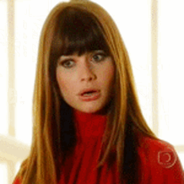 a woman with long brown hair and bangs is wearing a red turtleneck sweater .