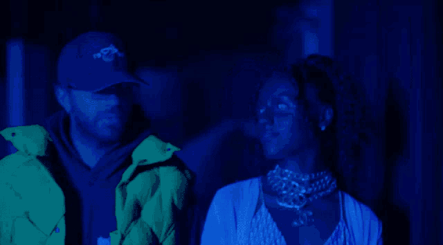 a man and a woman are standing in a dark room with a blue light behind them
