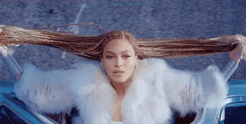a woman in a fur coat is sitting in a car and holding her hair .