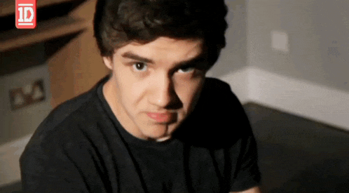 a young man in a black shirt looks at the camera with a 1d logo in the corner