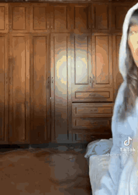 a woman in a white hoodie is standing in front of a wooden wardrobe .