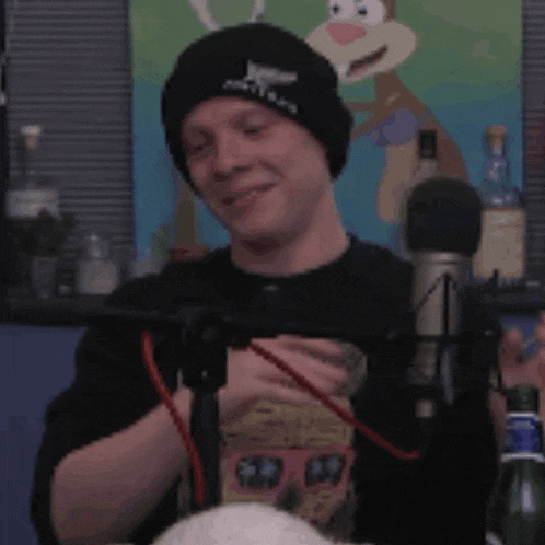 a man wearing a black beanie is covering his face with his hands while sitting in front of a microphone .