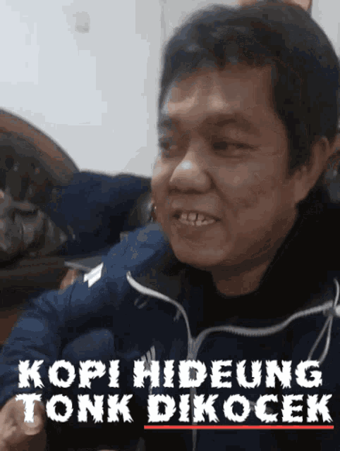 a man in a blue jacket is smiling with the words kopi hideung tonk dikocek above him