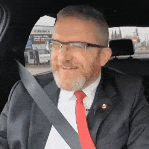a man wearing glasses and a red tie is sitting in a car
