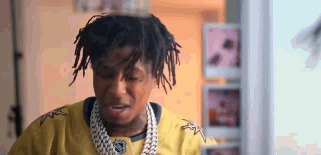 a young man with dreadlocks is wearing a yellow jersey and a gold chain .