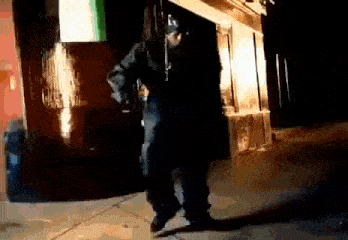 a man in a black jacket is dancing on the sidewalk in front of a building .