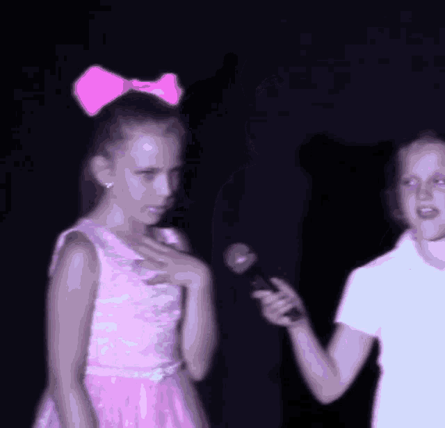 a girl in a pink dress with a pink bow in her hair stands next to another girl in a white shirt