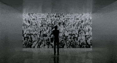a man stands in front of a wall with a large crowd of people on it