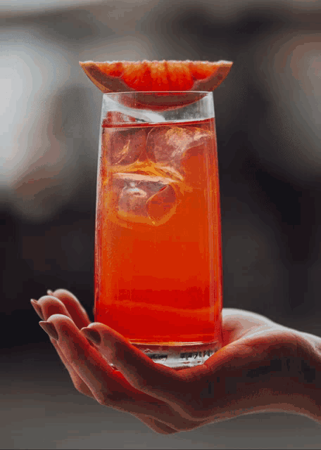 a woman holds a glass of orange juice with a slice of grapefruit on top