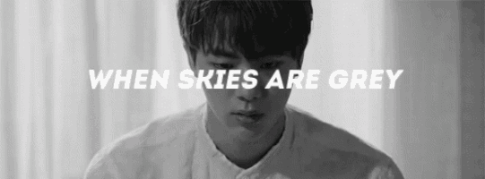 a black and white photo of a young man in a white shirt with the words `` when skies are grey '' written above him .
