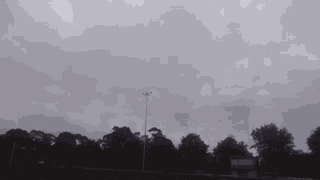 a cloudy sky with a few trees in the foreground and a building in the distance