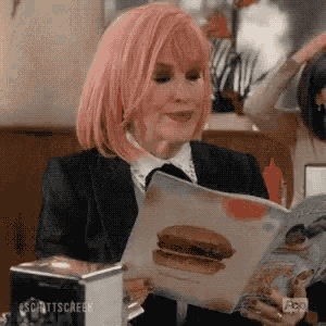 a woman with pink hair is reading a magazine with a picture of a hamburger .
