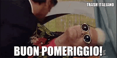 a man wearing sunglasses is laying on a bed with the words buon pomeriggio written above him .