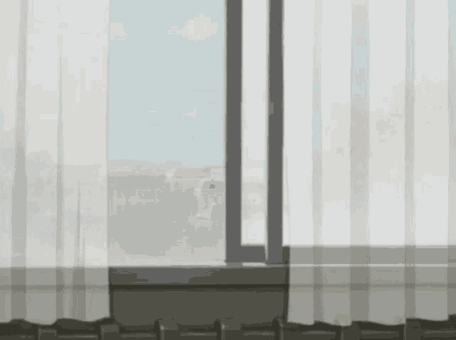 a window with a view of a city with a white curtain