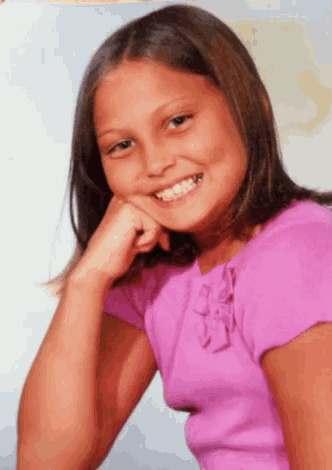 a young girl wearing a pink shirt is smiling with her hand on her chin
