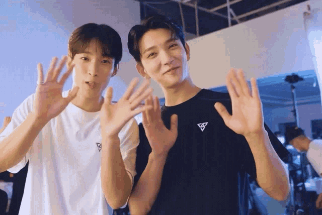 a man in a black shirt with a triangle logo on it stands next to another man in a white shirt
