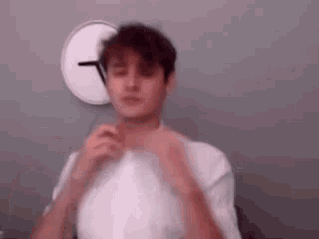 a man is adjusting his tie in front of a clock on the wall .