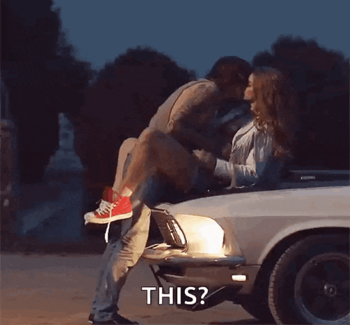 a man is holding a woman in his arms while kissing her on the hood of a mustang .