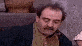 a man with a mustache is wearing a scarf around his neck and looking at the camera .