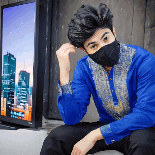 a man wearing a blue shirt and a black mask is sitting in front of a television