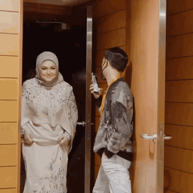 a woman in a hijab smiles while standing next to a man in a sweater