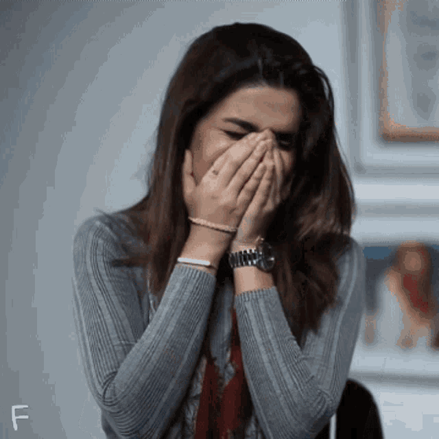 a woman covering her face with her hands and the letter f is visible in the corner