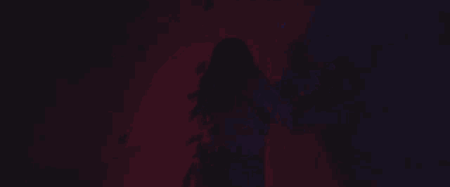 a woman is standing in front of a wall in a dark room in a purple light .