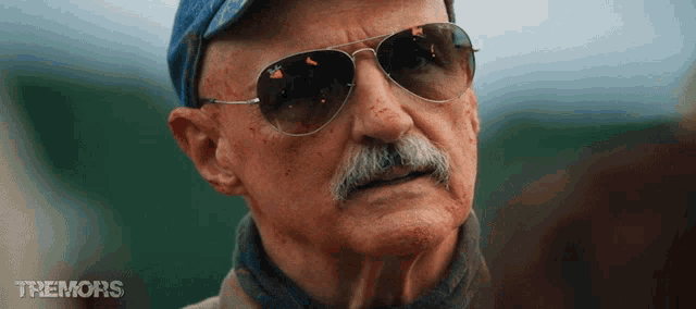a man with a mustache wearing sunglasses and a hat with the word tremors on the bottom