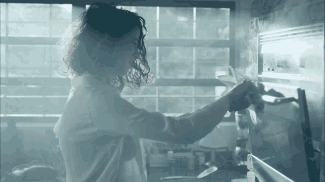 a woman in a white shirt is taking something out of a oven