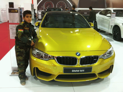 a young boy standing next to a yellow bmw m4