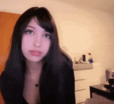 a woman with long black hair and green eyes is standing in a room looking at the camera .