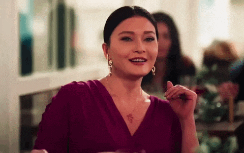 a woman in a purple dress and earrings is sitting at a table with other people .