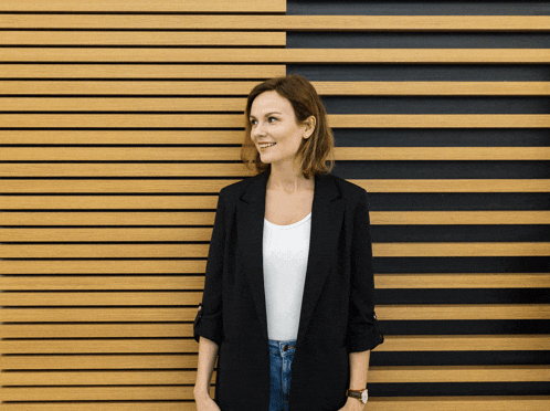 a woman standing in front of a wooden wall wearing a black jacket