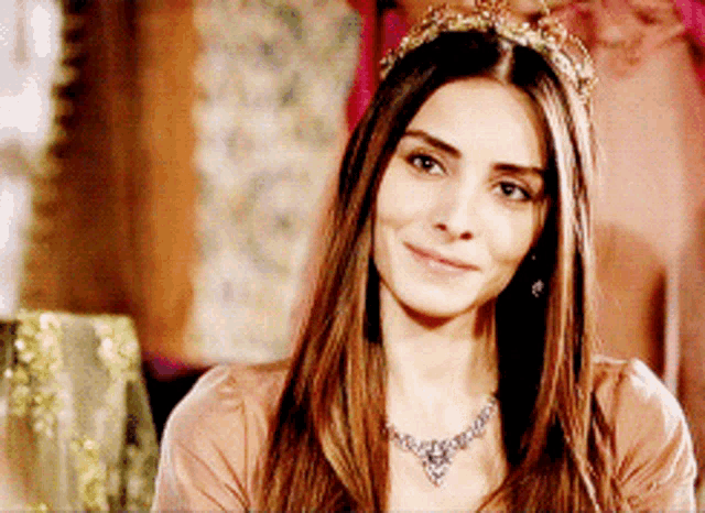 a woman wearing a tiara and a necklace smiles at the camera