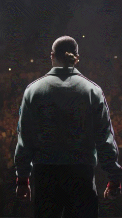 a man in a green adidas jacket stands in front of an audience