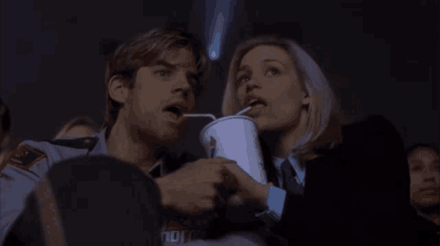 a man and a woman are watching a movie and the man is drinking through a straw from a cup that says coca cola