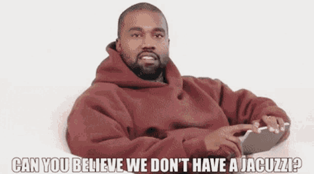 a man in a red hoodie is sitting on a couch with a cell phone in his hand .