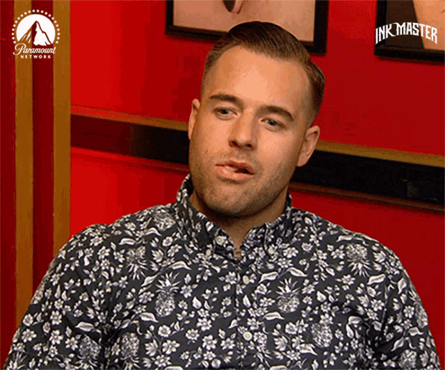 a man in a black and white floral shirt is sitting in front of a paramount network sign