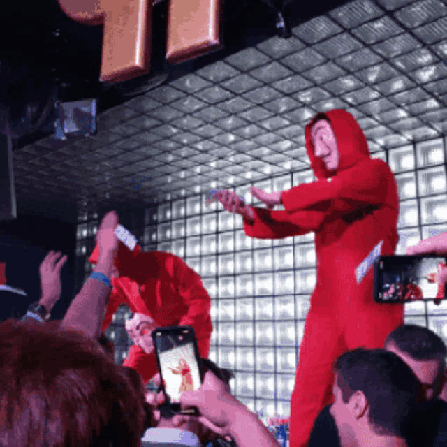 a man in a red jumpsuit stands in front of a crowd of people taking pictures