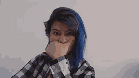 the woman is wearing a plaid shirt and has blue hair .