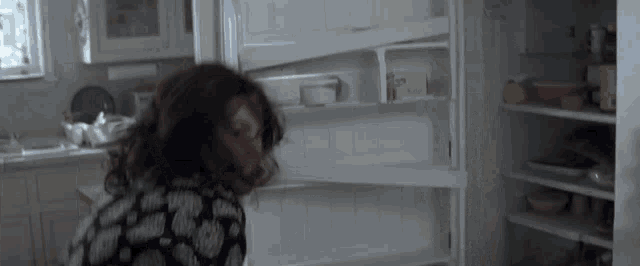 a woman is standing in front of an empty refrigerator looking for something to eat ..