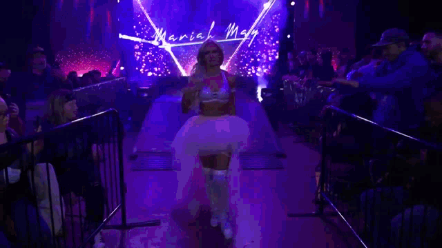 a woman in a tutu is walking through a ring with the name mariah mcgraw written on the wall behind her