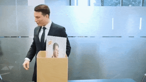 a man in a suit and tie is holding a cardboard box with a picture of a man on it